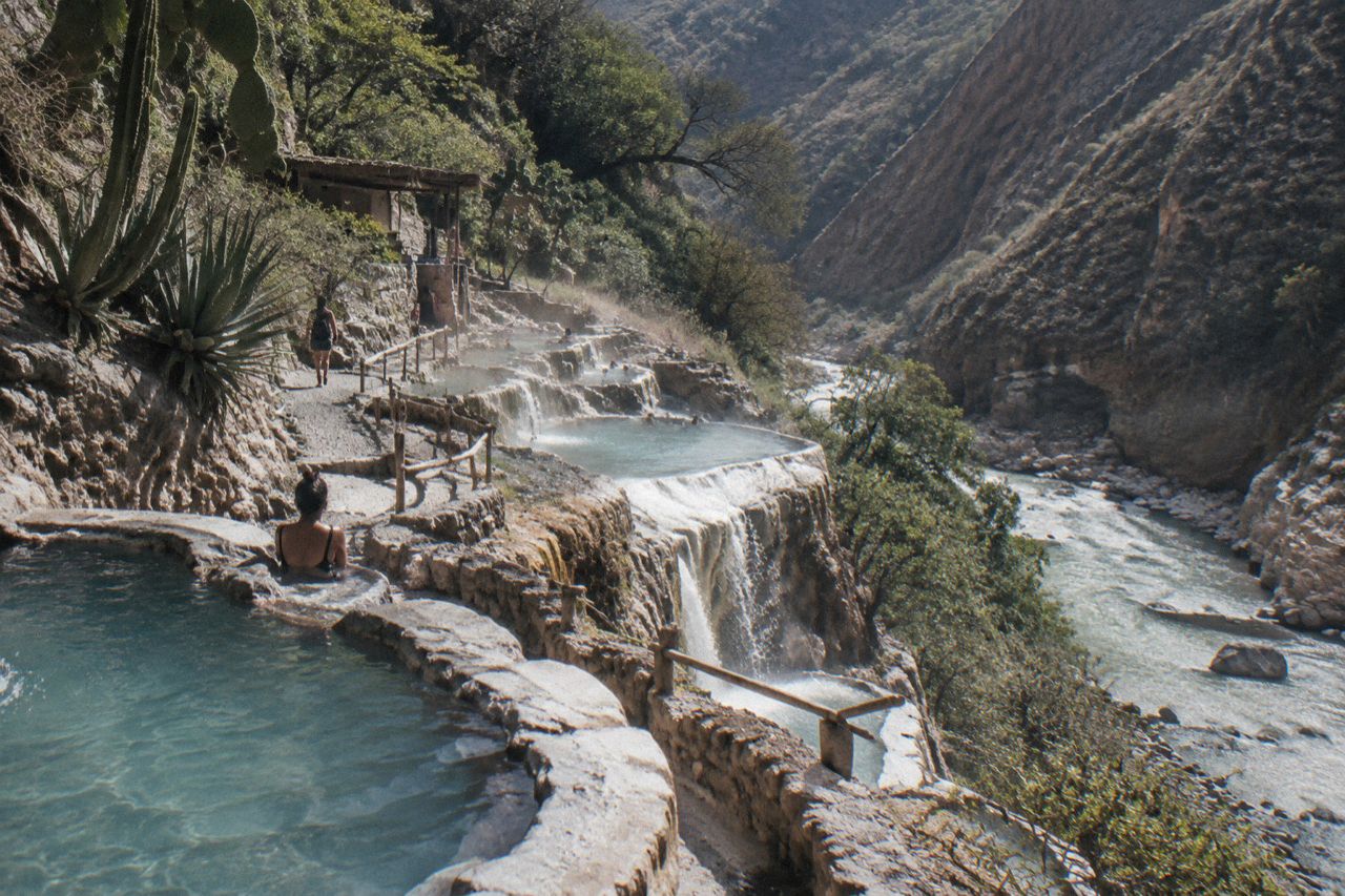 Hillside thermal pools overlooking forested mountains and a river valley in rural Mexico