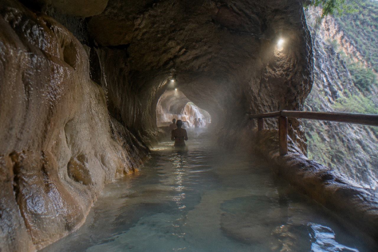 Steam rising from a warm pool inside a rocky cave with a narrow tunnel opening in Mexico