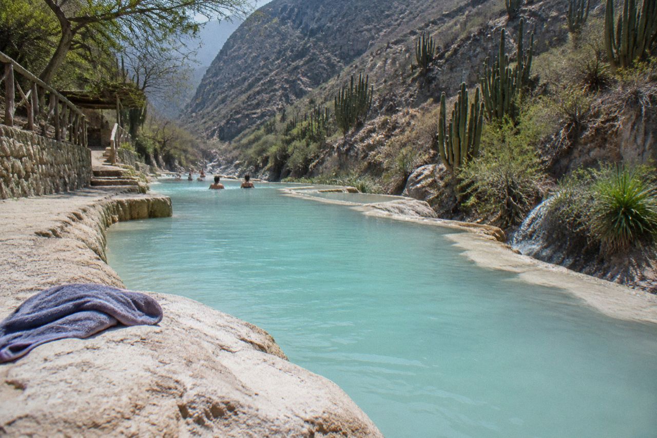 Visitors wading in a warm turquoise river between steep rocky canyon walls in Mexico